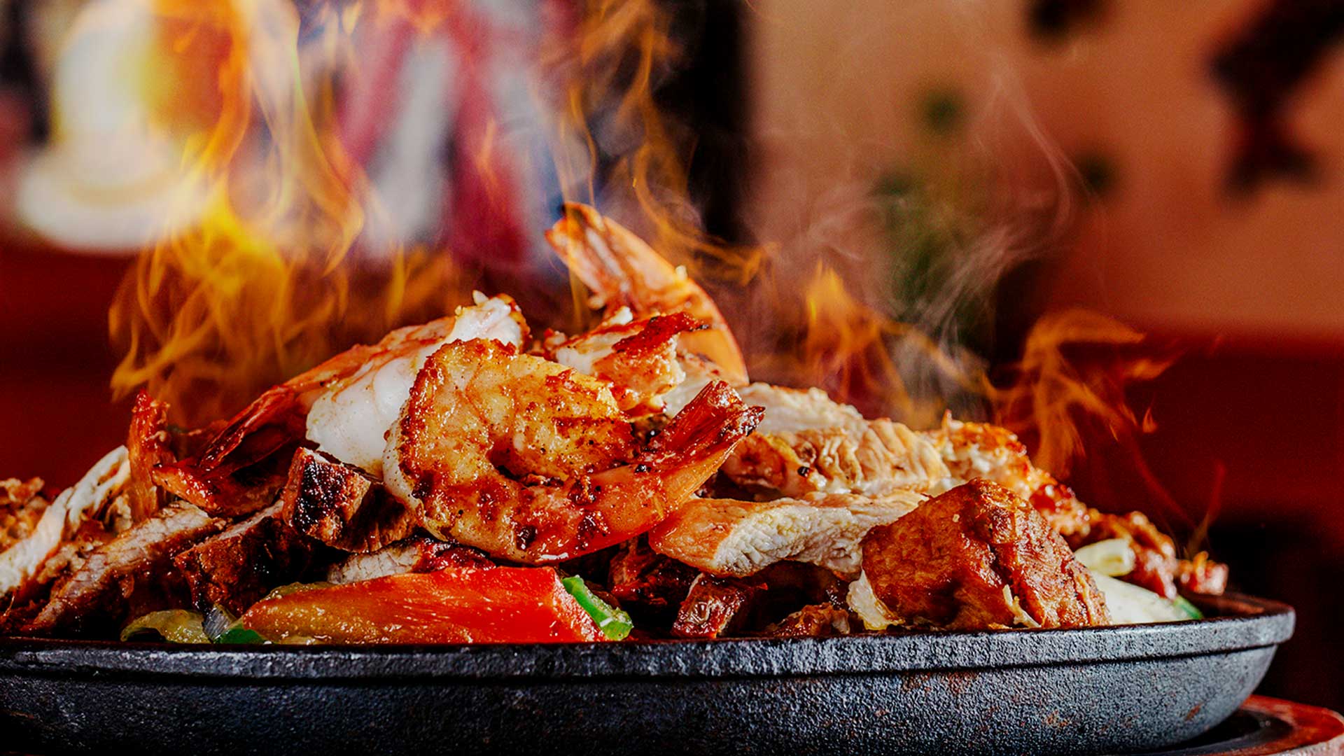 A flaming fajita topped with shrimp, one of the delicious Mexican food specialties we offer