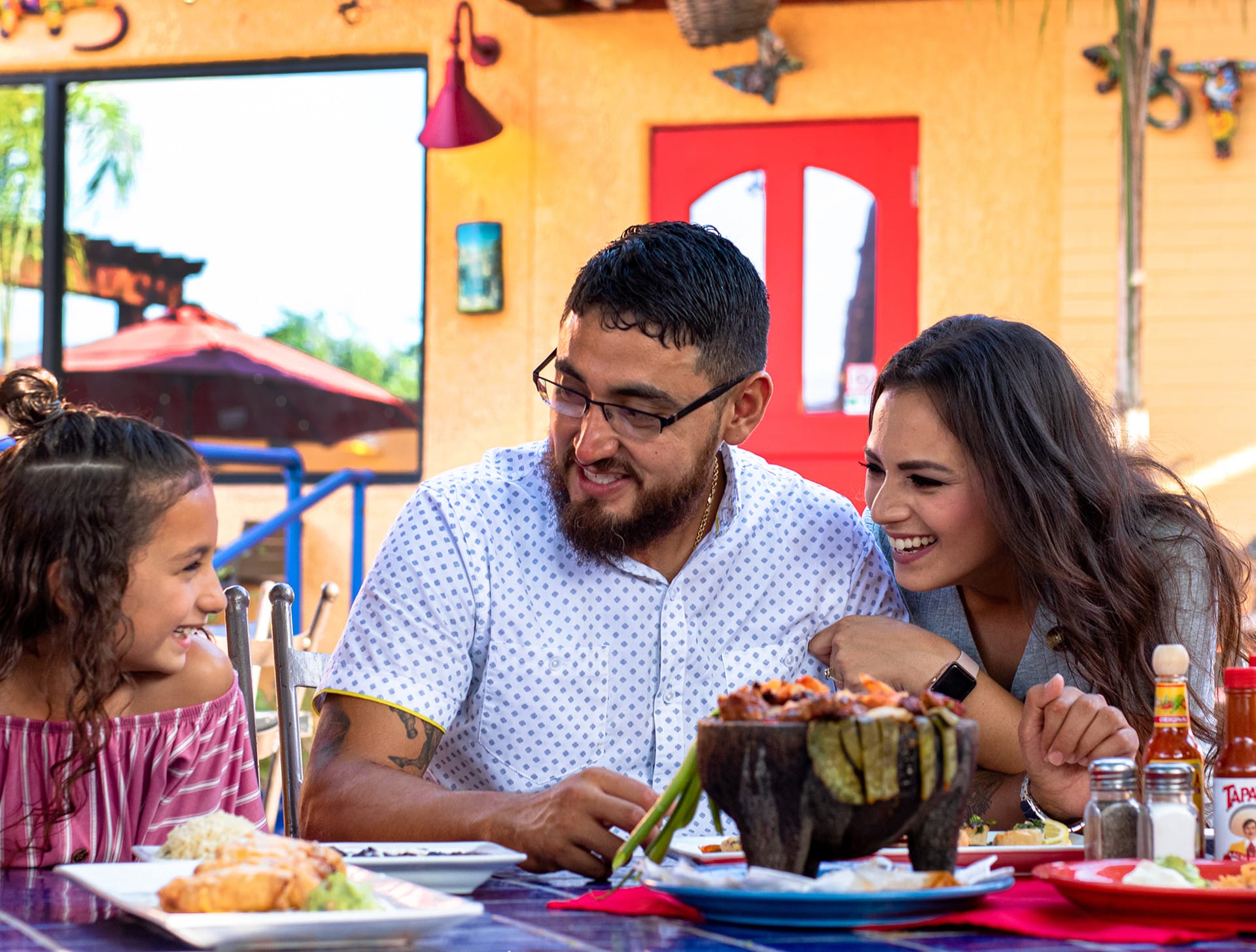 Parents laughing with their young daughter while enjoying a molcajete